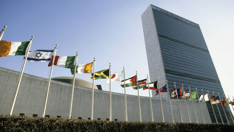 View of the United Nations Headquarters. Flags from different nations floating on flag polls. Tall building representing the UN Secretariat.