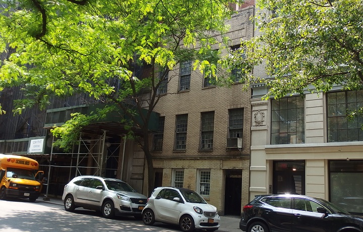 Outside of Julius' Bar; a short sand colored building, a rainbow flag sticking o
                                           