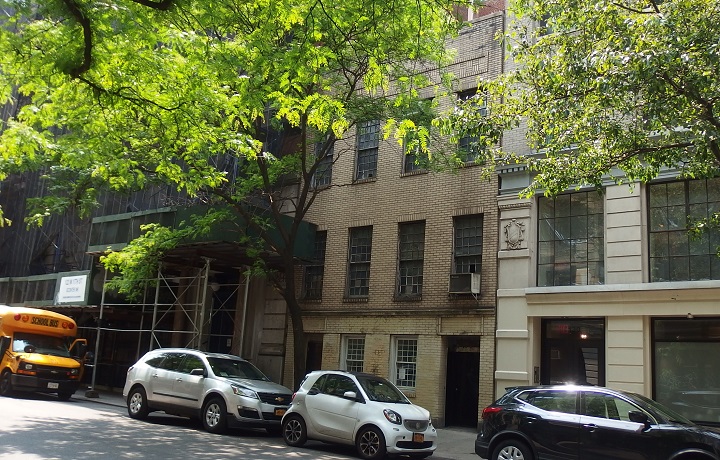 A construction scafold, an abundant colored school, and cars park at the side of the road