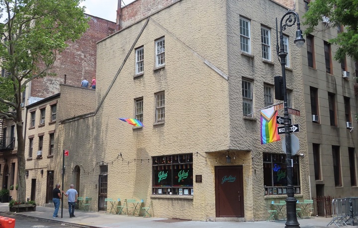 Outside of Julius' Bar; a short sand colored building, a rainbow flag sticking o
                                           