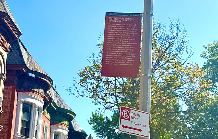 Color photo of a red sign mounted high on a pole with historic row houses in the background
                                           