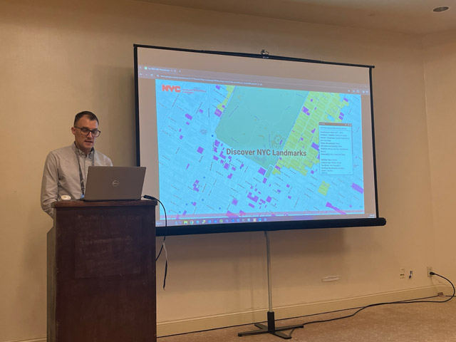 Man speaking at podium. Screen next to him displays part of a map of Manhattan and reads “Discover NYC Landmarks”