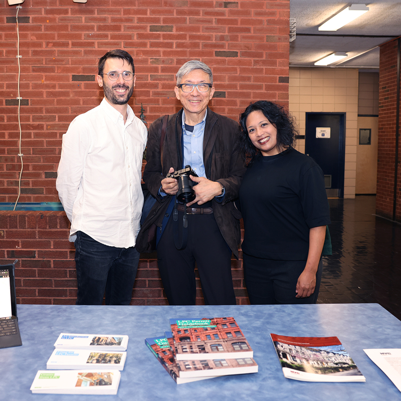 Three smiling people stand in front of a table.  Photo courtesy of Susan Soo