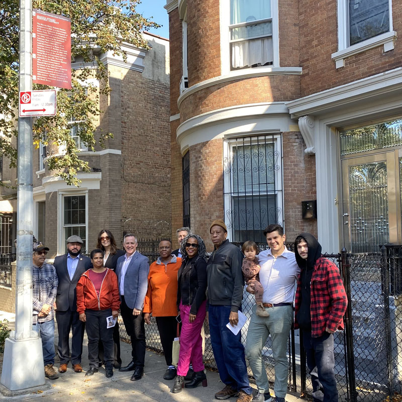 Group of smiling people on sidewalk next to pole with historic district marker