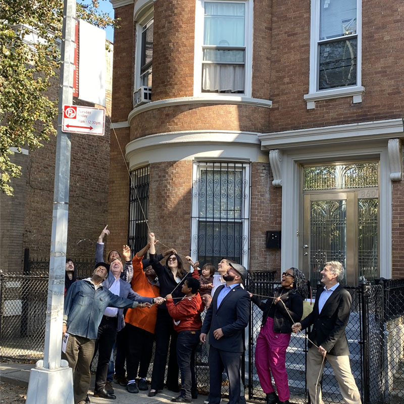 Group of people on sidewalk pulling cover off historic district marker mounted on pole