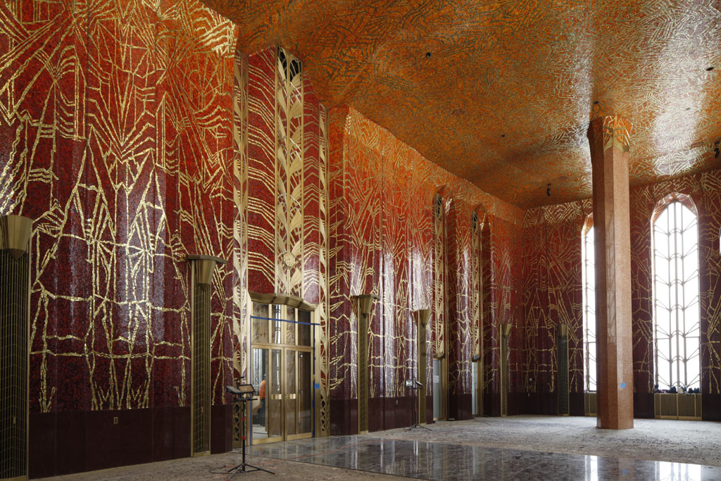 Red room with high ceilings and pillars, walls and ceiling covered with red mosaic tile with gold designs. 