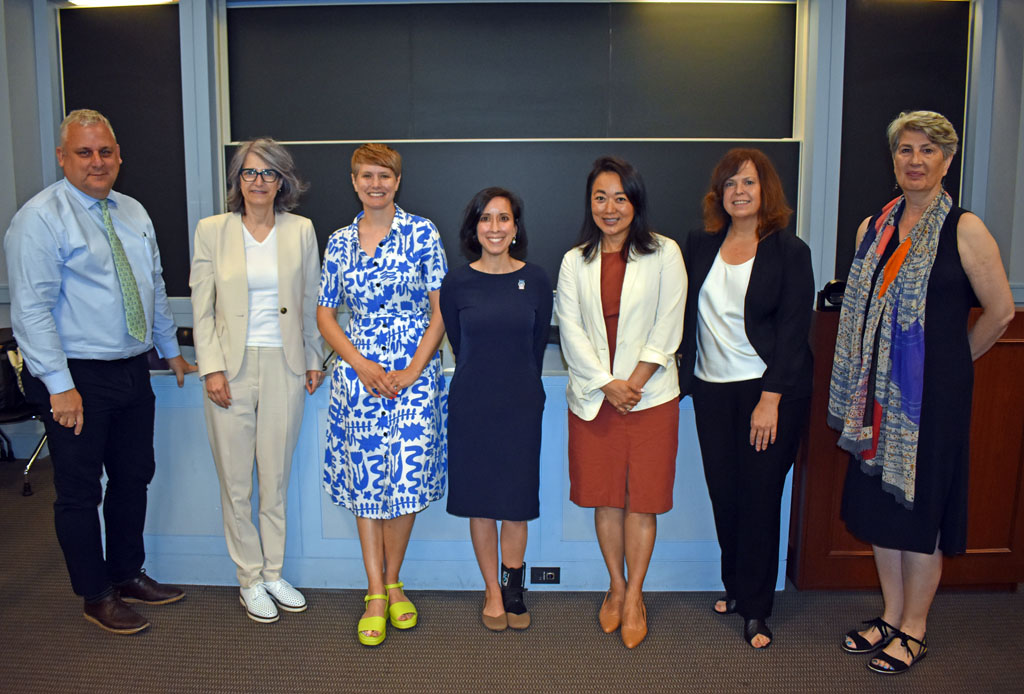 Smiling people standing in front of a desk with blackboard in background