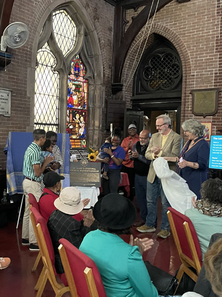 People standing and seated in a church, looking at a plaque and clapping