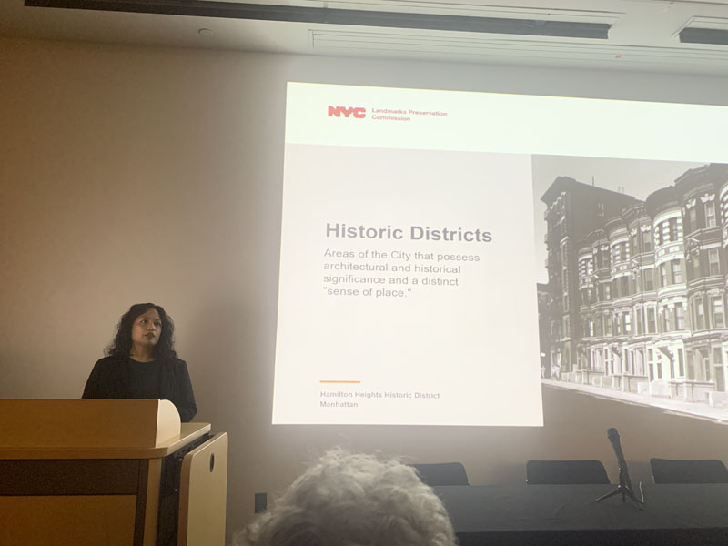 Person speaking while standing behind podium with a screen in the background, text on the screen reads: Historic Preservation: Areas of the City that possess architectural and historical significance and a distinct sense of place