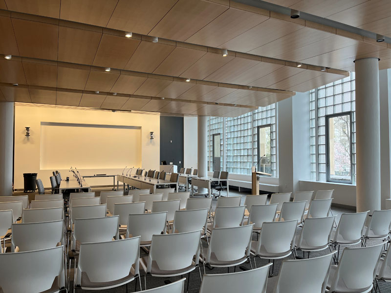 large room with chairs and a podium in the forefront of photo, and long tables with microphones in the background
