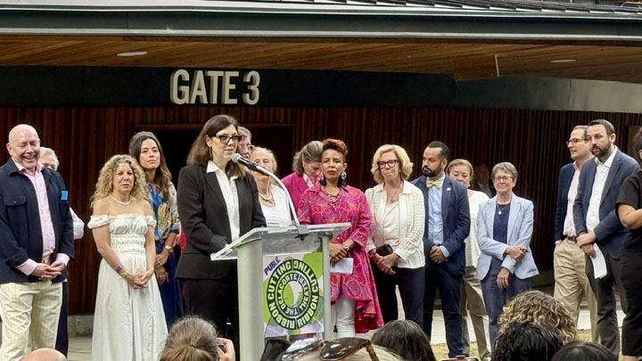 Person speaking at a podium while others stand in the background