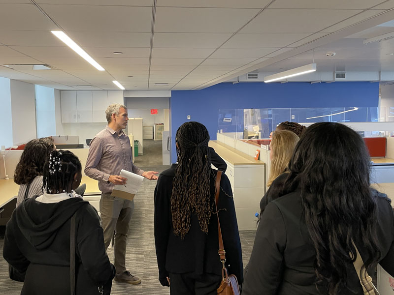 : Person speaking to a group of people, surrounded by cubicles