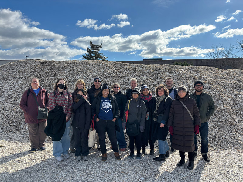 Group of people stand in front of large pile of oyster shells