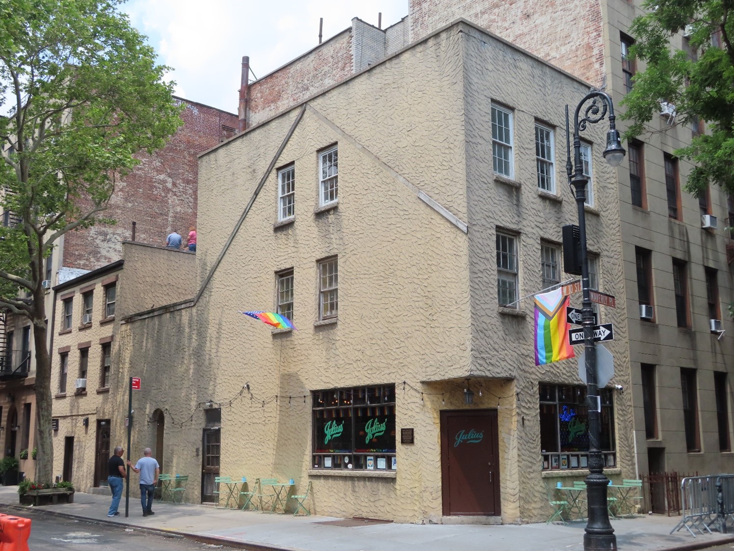 Outside of Julius' Bar; a short sand colored building, a rainbow flag sticking out a window