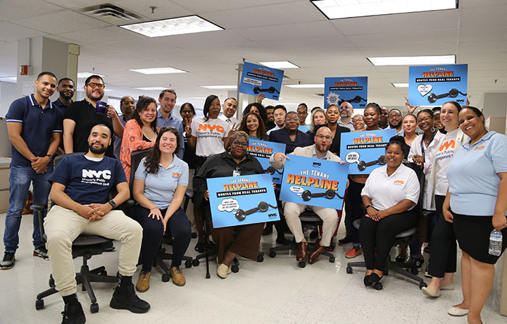: Large group of PEU staff smiling, wearing PEU shirt, and holding signs that sa
                                           