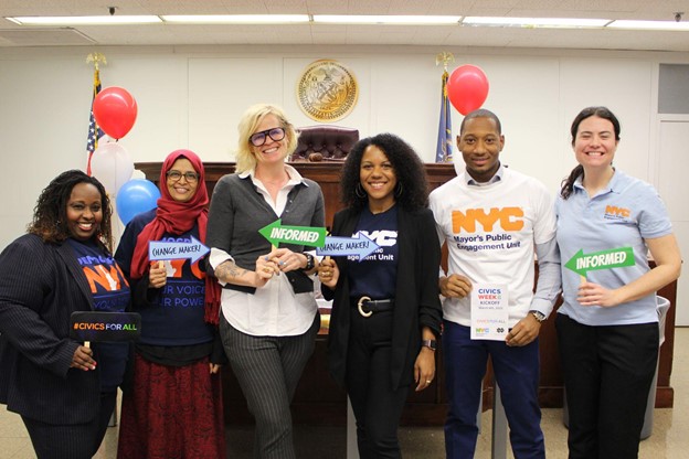 Six people stand and pose for the camera, smiling, and holding different signs