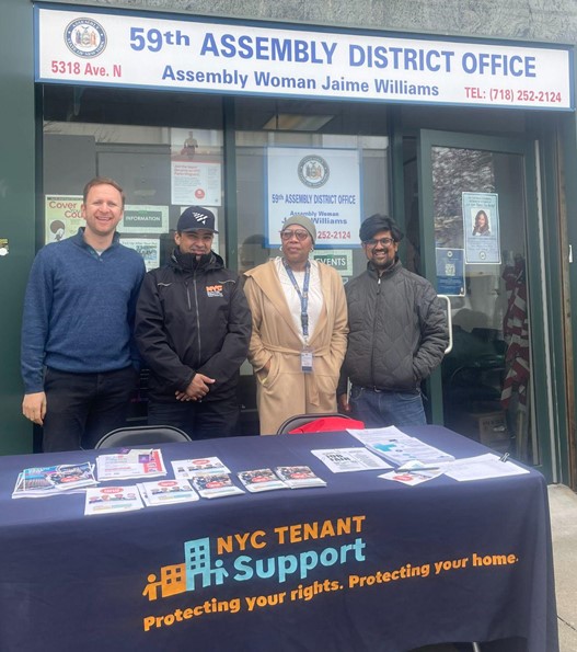 Tenant Support Unit stand behind table posing for the camera. The table cloth reads 'NYC Tenant Support. Protecting your rights. Protecting your home'. There are multiple flyers on the table.