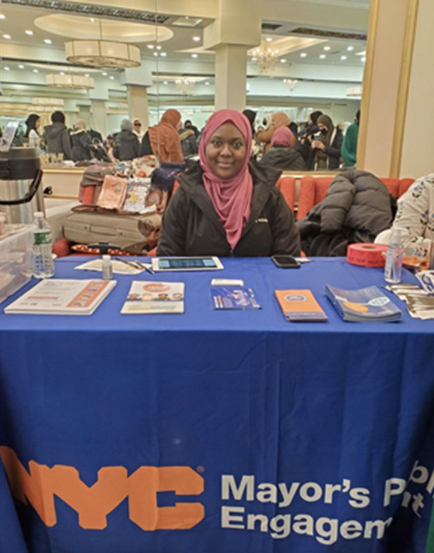 Photo of a GetCoveredNYC Specialist, she sits at a table with health care flyers and brochures in front of her.