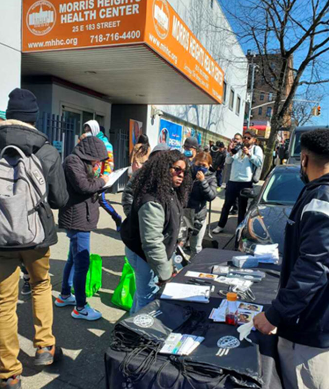 PEU staff outside in sunny weather.  Many people are outside and one woman can be seen interacting with PEU staff member in front of a table with flyers
