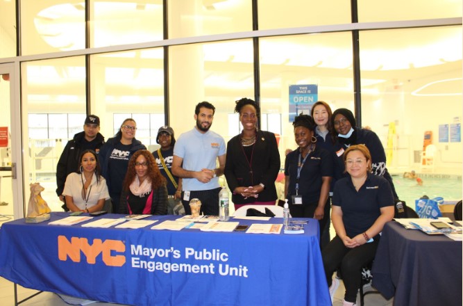 PEU staff with Bronx BP stand behind table smiling as they pose