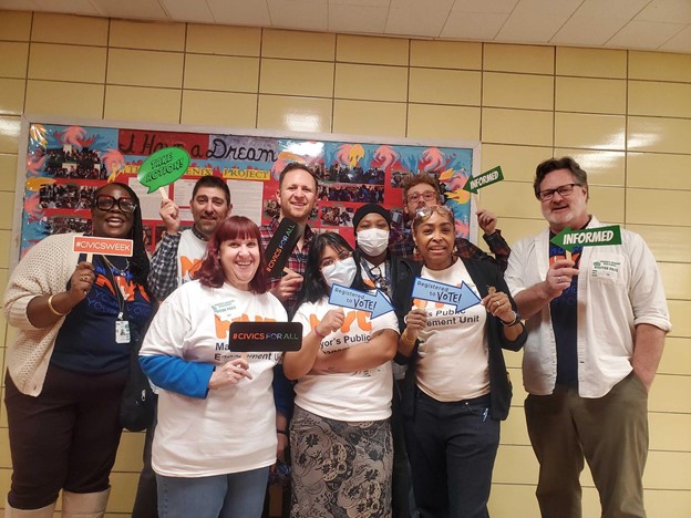 Staff all stand together smiling at the camera holding signs.