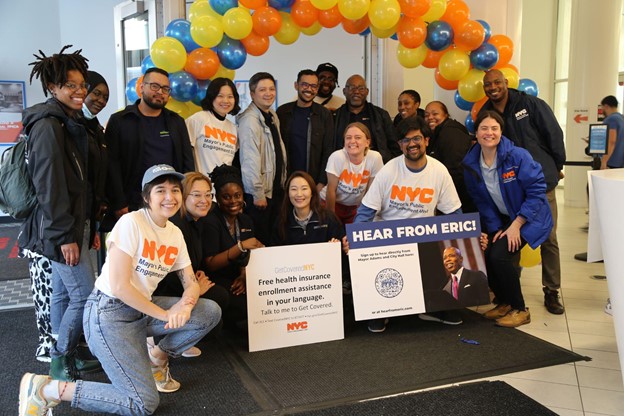 PEU staff gathers together with Bronxnet staff in front of colorful balloon arch while holding signs that read 