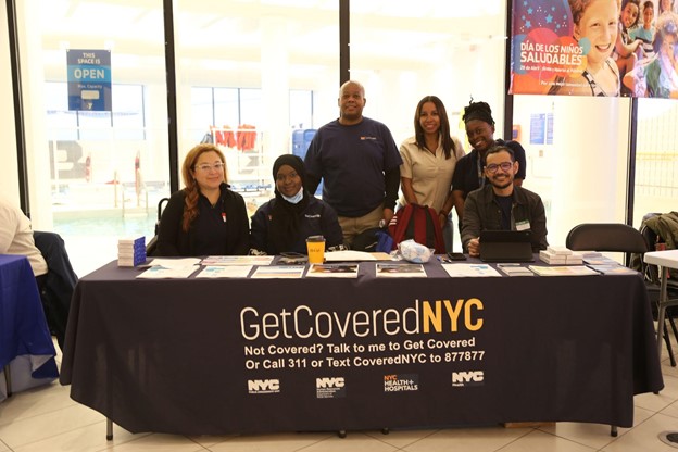GetCoveredNYC team behind table with table cloth that reads 'GetCoveredNYC'. Table has a lot of flyers.