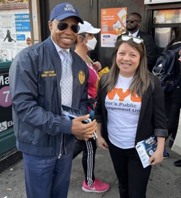 P E U staff member poses on the sidewalk with Mayor Adams in front of the train station
