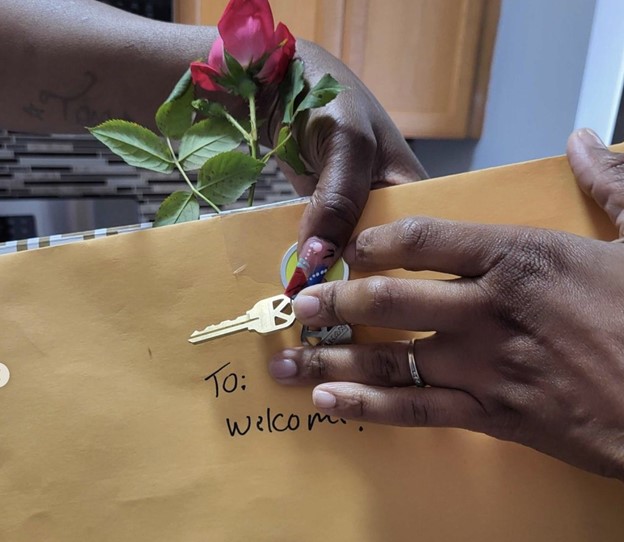 Two hands overlap and hold a pair of keys over a manila folder