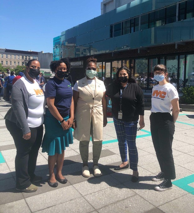 Five women stand outside posing for the camera wearing masks.