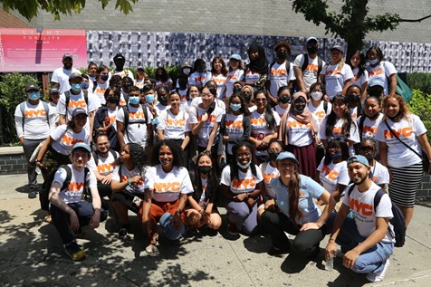 A group of CUNY interns gathered together outside with the Mayor's Public Engagement unit staff, all wearing PEU T-shirts. 