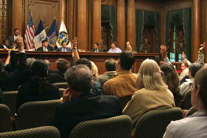 Photo of people raising their hands at a hearing.