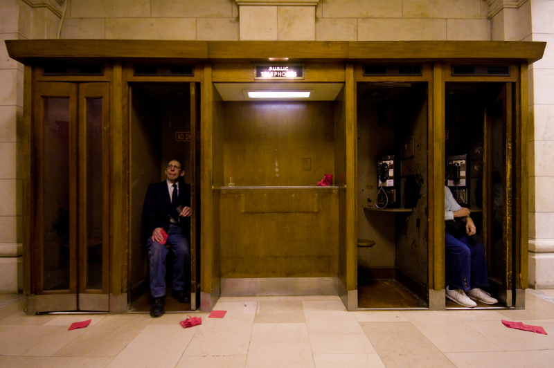 Photo of two people sitting in public phone booths.