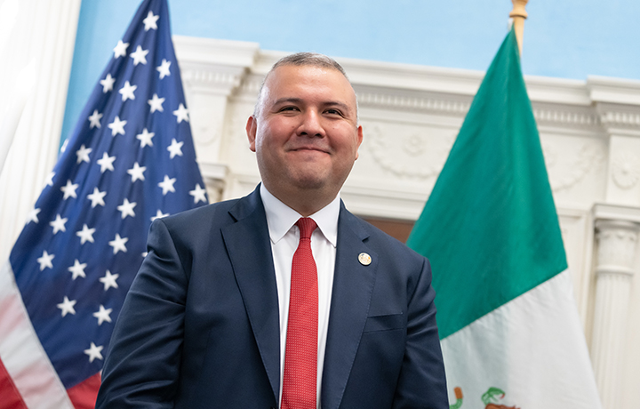 Commissioner Manuel Castro smiling in front of a United States flag and a Mexican flag
