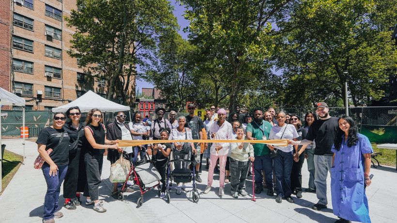 Newly transformed community space at Roosevelt Houses, featuring modern wooden bench seating, newly installed large rectangular planters with green plants, and a paved walkway.
                                           