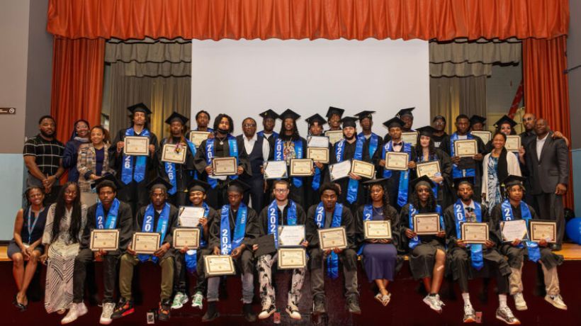 YouthBuild program graduate Nasir Hayes-Jones posing proudly with a graduation certificate alongside program supervisors and fellow graduates following a six-month construction training program.
                                           