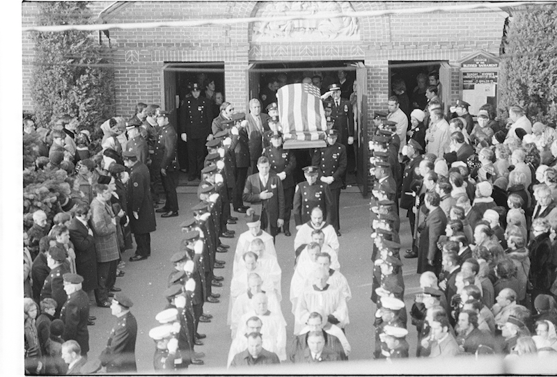 Funeral processsion outside church, police officers carrying flag-draped coffin