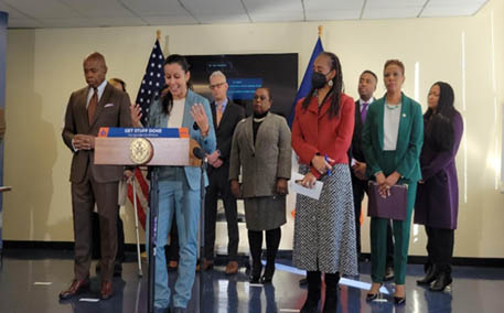 Group of people with Mayor Eric Adams standing at podium with speaker for signing of NYC bills into law