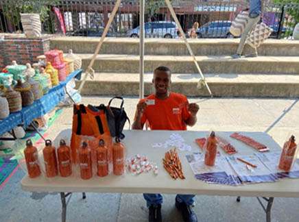 A person sitting at a table with giveaways in an outdoor courtyard.
