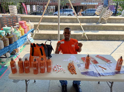 A person sitting at a table with giveaways in an outdoor courtyard.
