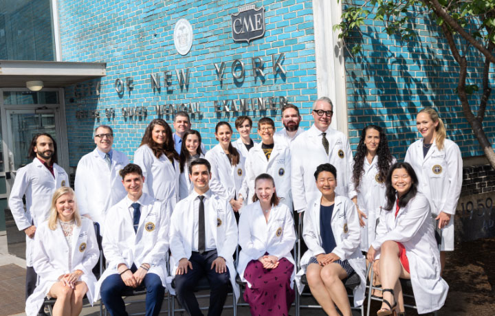 Several people wearing white lab coats in front of the OCME building
                                           