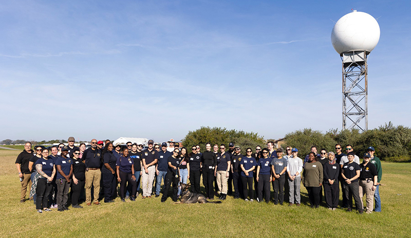 A large group of medical examiners and other OCME specialists stands with agency K-9 Raven and colleagues from partner government agencies during training exercise at Floyd Bennett Field in Brooklyn, New York. 