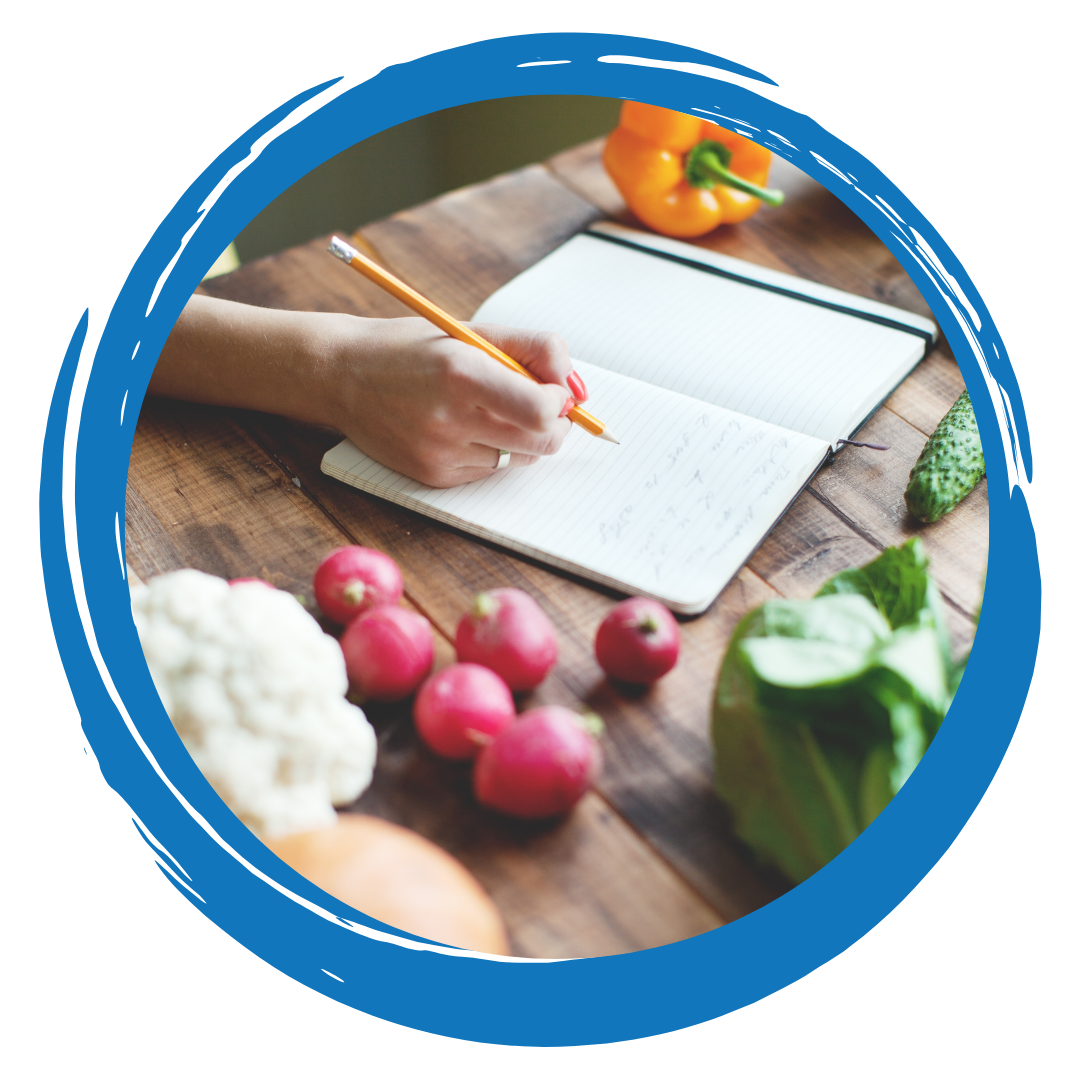 Person writing in a notebook with vegetables on the table