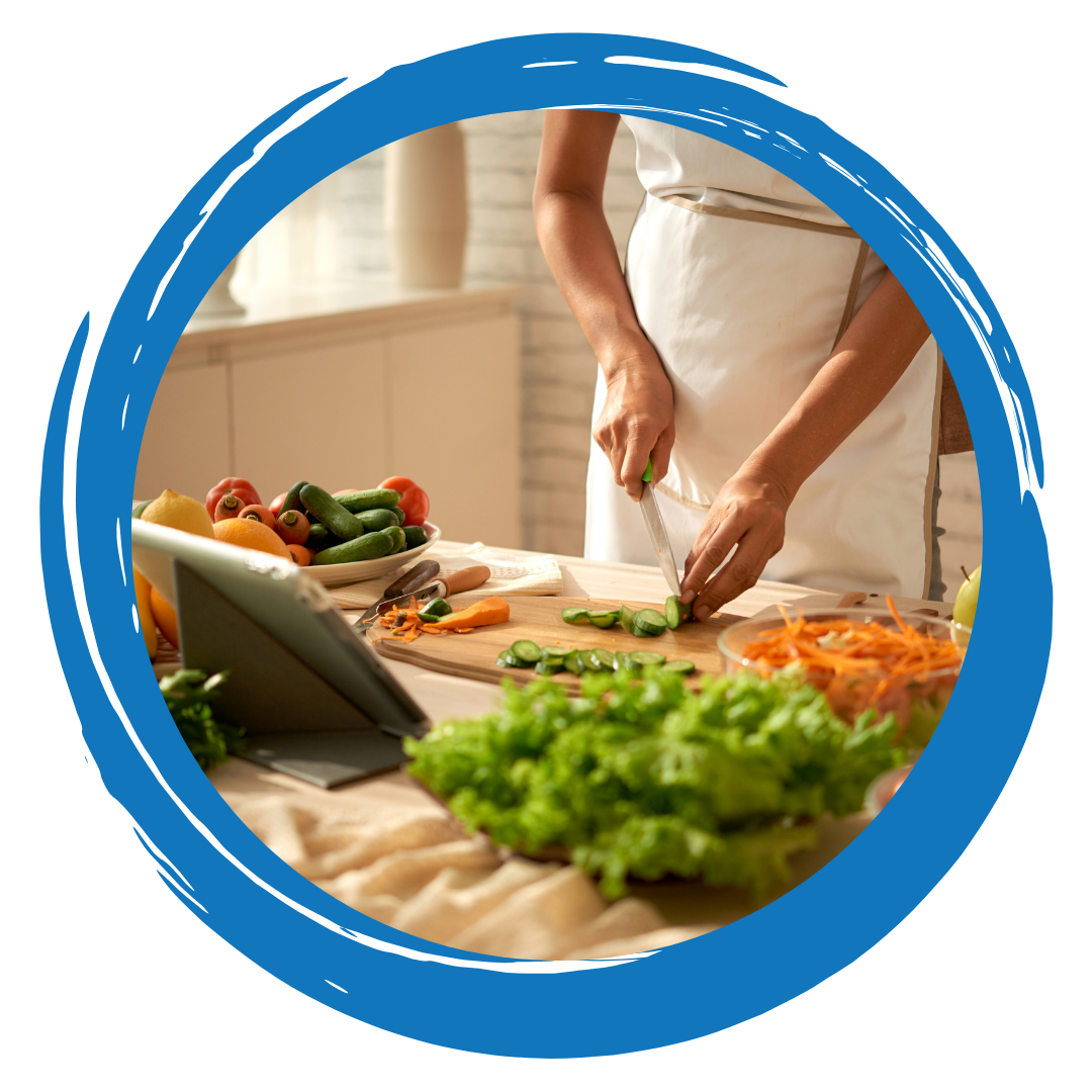 A person chopping vegetables while looking at a tablet