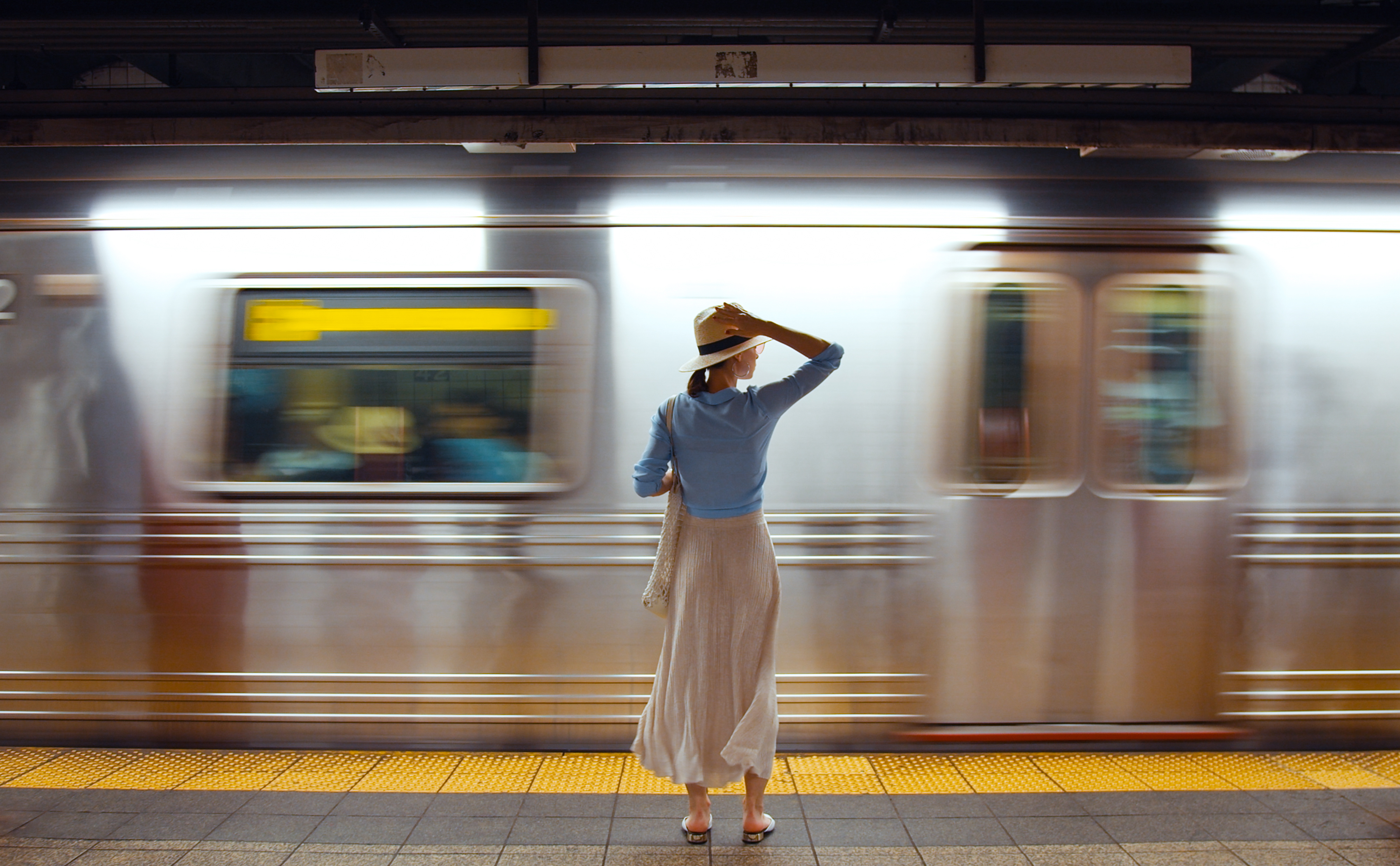 This is an image of a New York City subway with a woman standing on the platform.
                                           