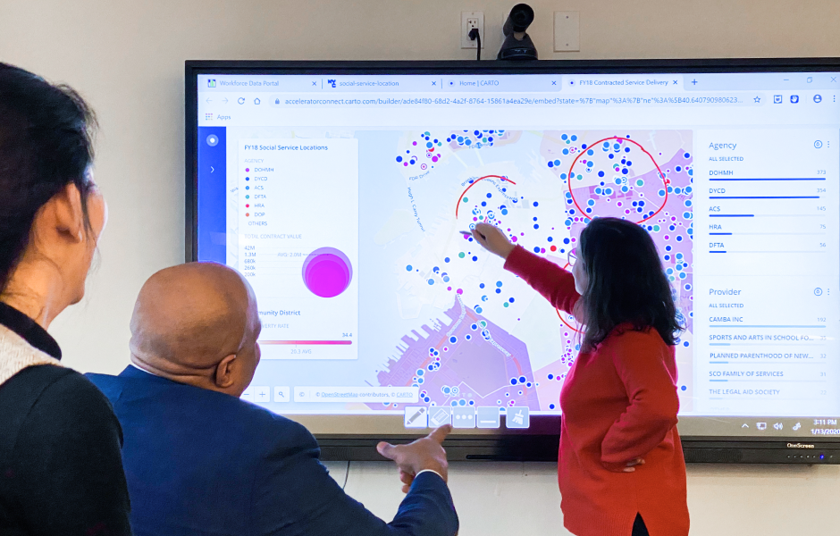 Woman in red sweater circling social services site locations on a map projected on a large screen.