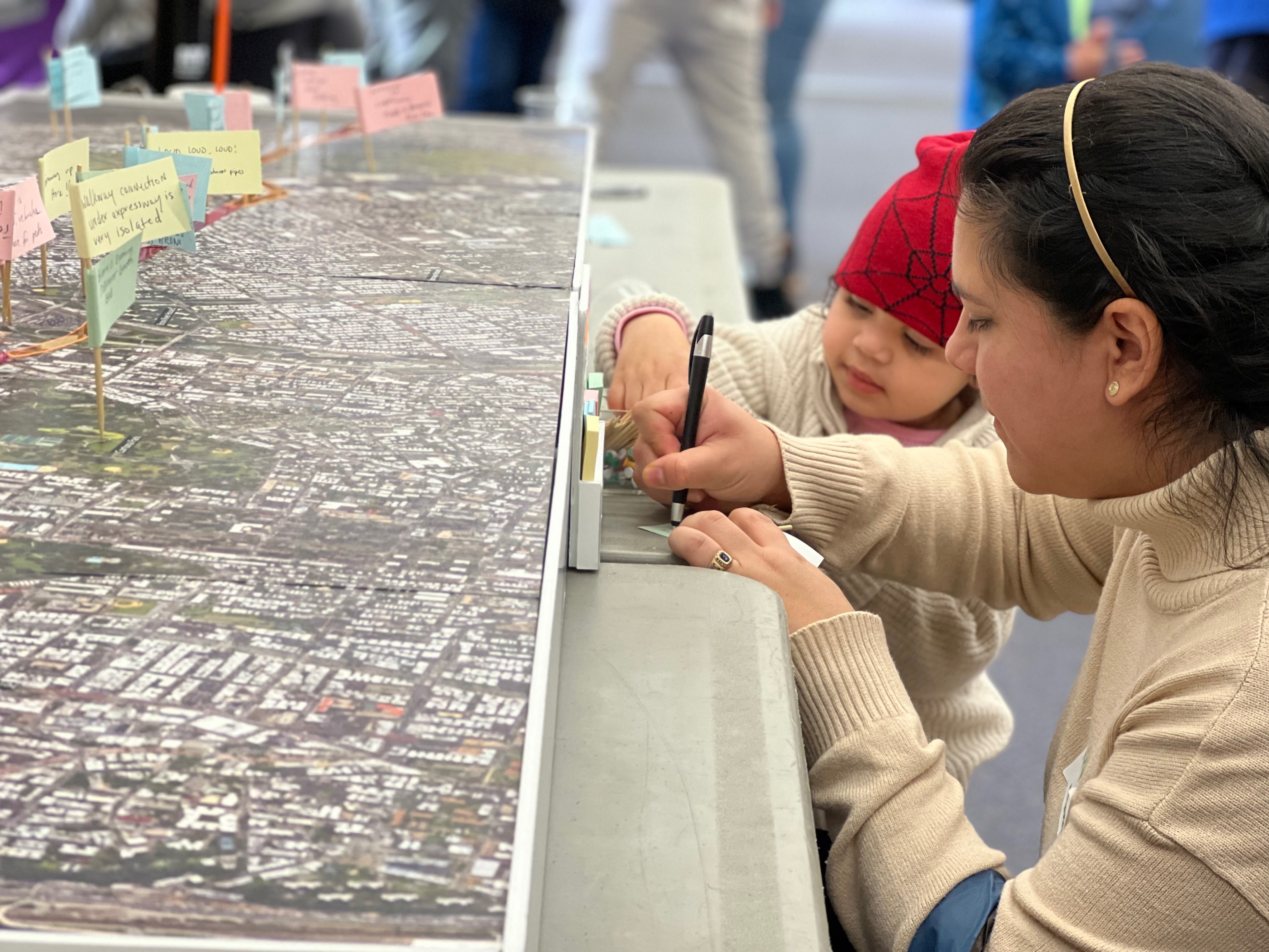 A woman and child write together on a post-it note at a community engagement event