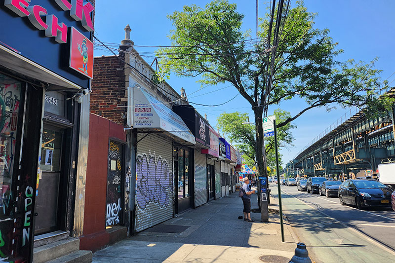 White Plains Road with 1 story commercial building, protected bike lane and elevated train tracks