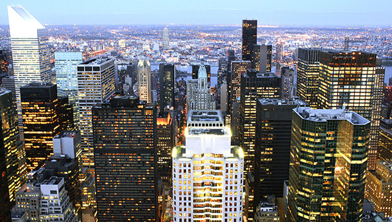 A shot of office buildings in east Midtown with lights on as the sun sets.