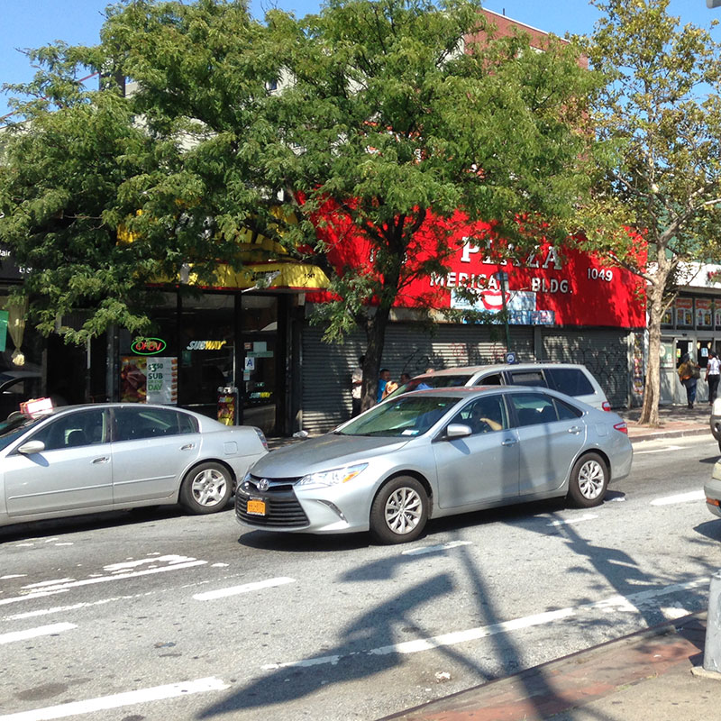 Silver sedan passing storefronts and parked cars